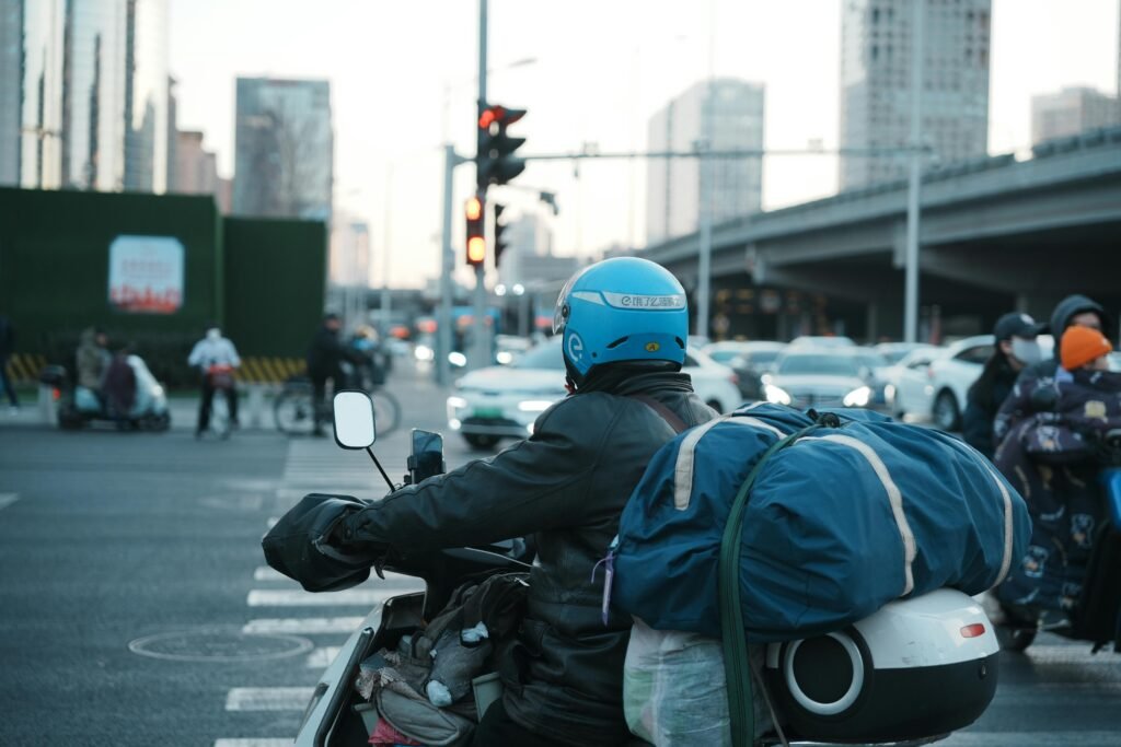 Motorcycle rider with helmet carrying large bag in busy city intersection.